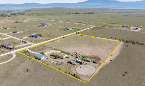Aerial view of a yellow-outlined rural property with houses, sheds, vehicles, and a large circular tank nearby.
